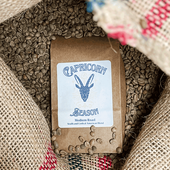 Bag of North Koffee Capricorn Seasons on top of green coffee beans in a jute bag.