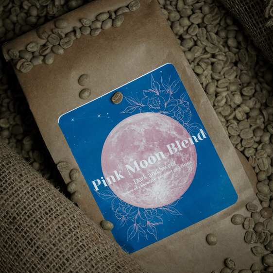 Bag of Pink Moon Blend coffee surrounded by green coffee beans